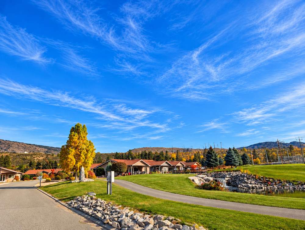 Landscaped pond with a small waterfall, a paved walking path, lawn and tile-roofed homes beside the road at Canyon Desert Golf Villas