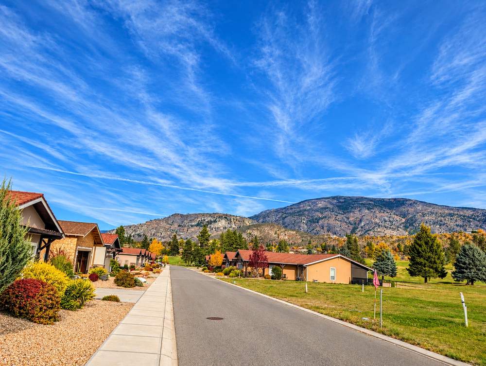 Paved street at Canyon Desert Golf Villas with stucco homes on one side and open lawn on the other, hills behind