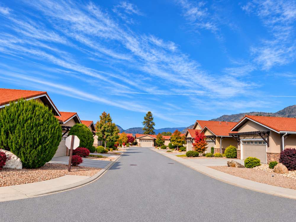 Street at Canyon Desert Golf Villas with stucco homes, red tile roofs, timber pergola entries, garages and a stop sign